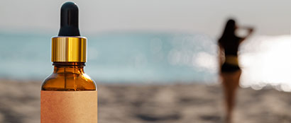 A woman on the beach in the distance with a bottle of after sun care in the foreground