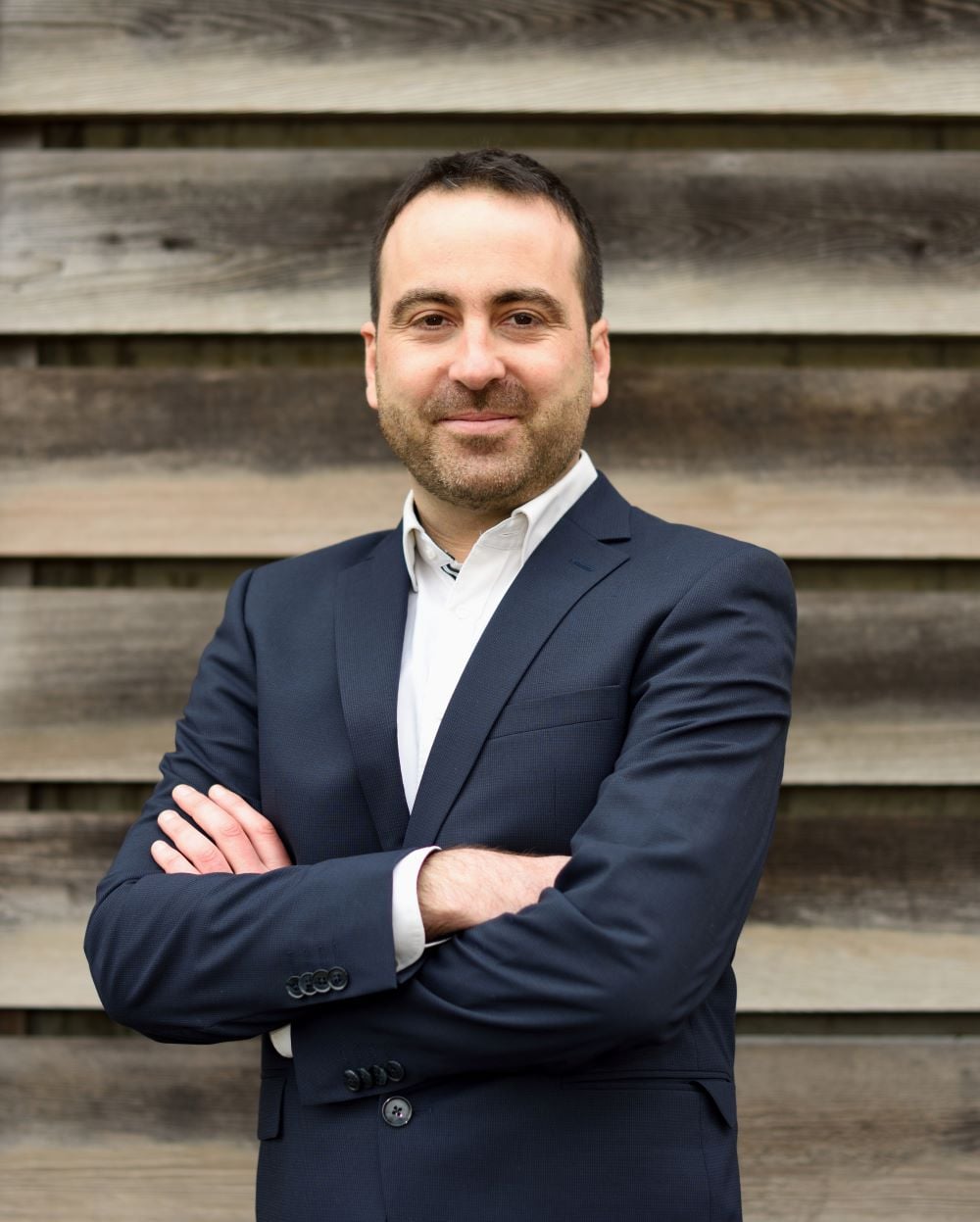 smiling, well-dressed man in front of stairs with his arms folded