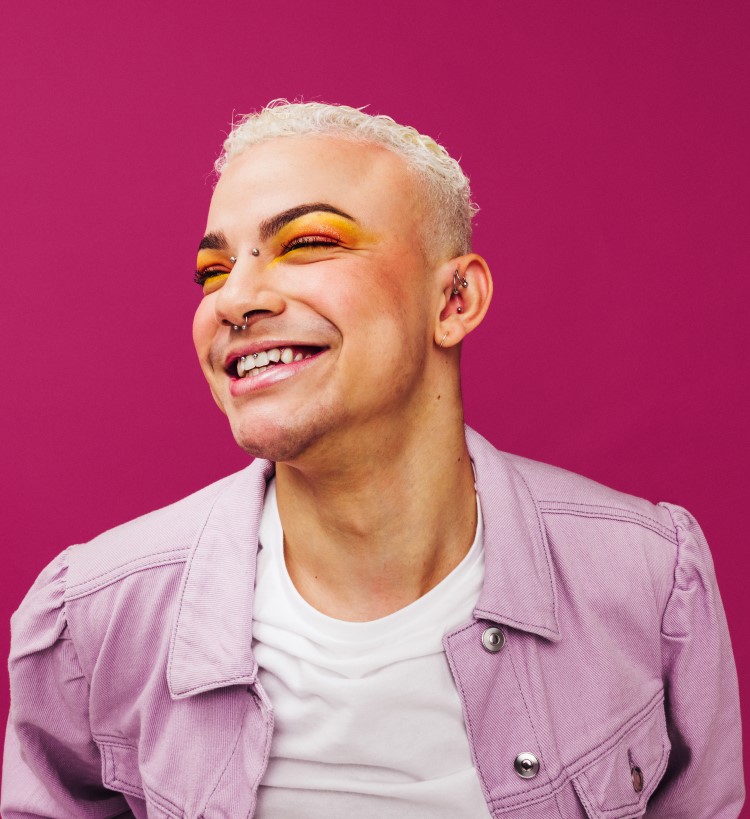 A gender nuetral person wearing a tiara and inclusive beauty formulations smiles