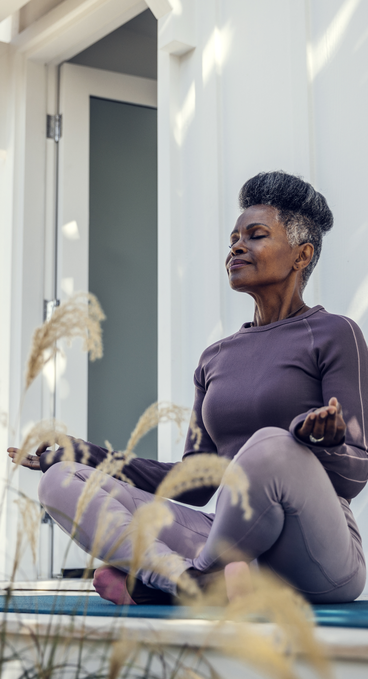 An older woman sitting cross-legged outdoors practicing yoga.