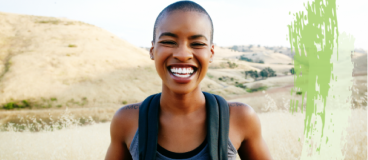 img title A younger woman wearing a backpack smiling with mountains and trails in the background